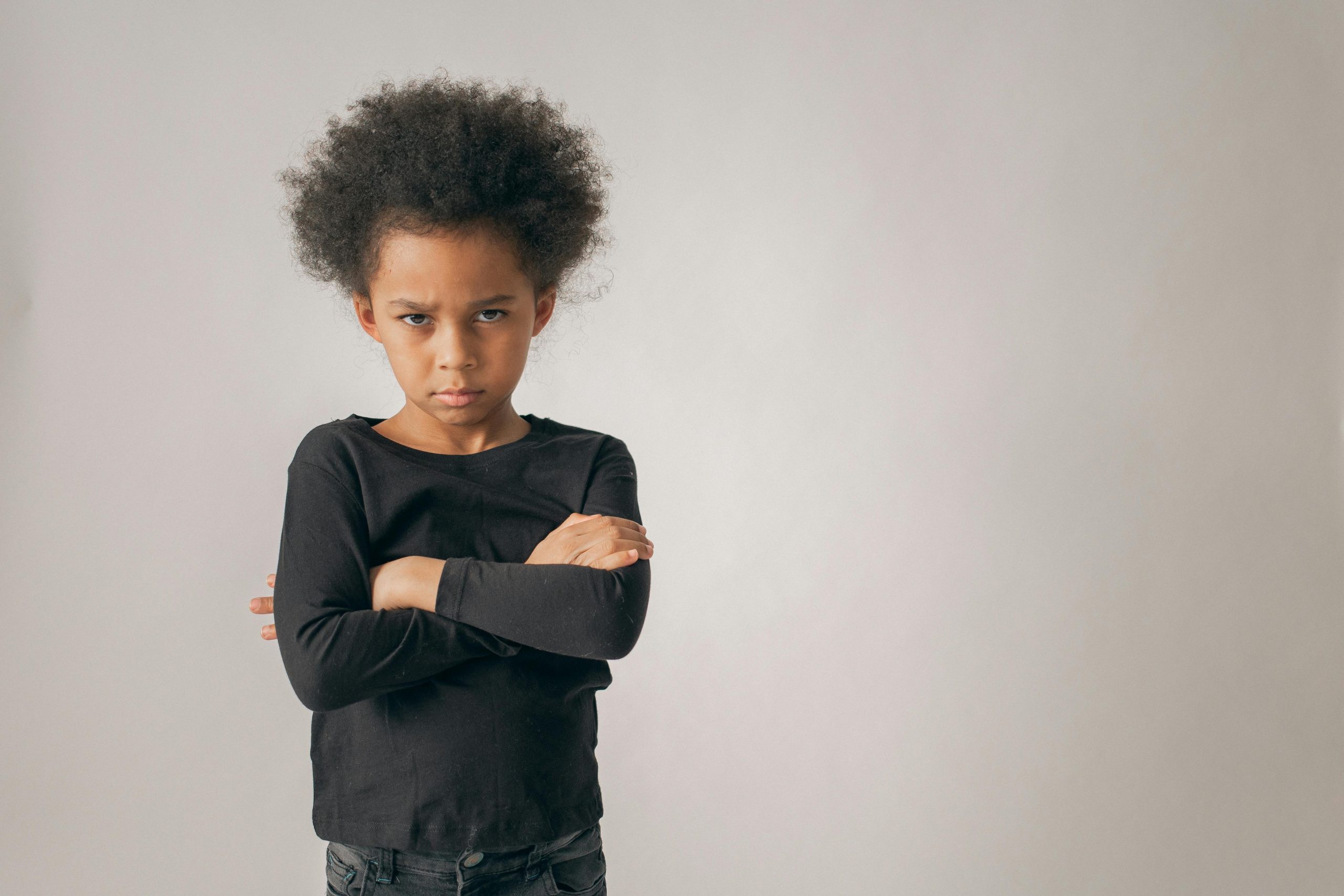 angry little girl frowning and standing with her arms crossed