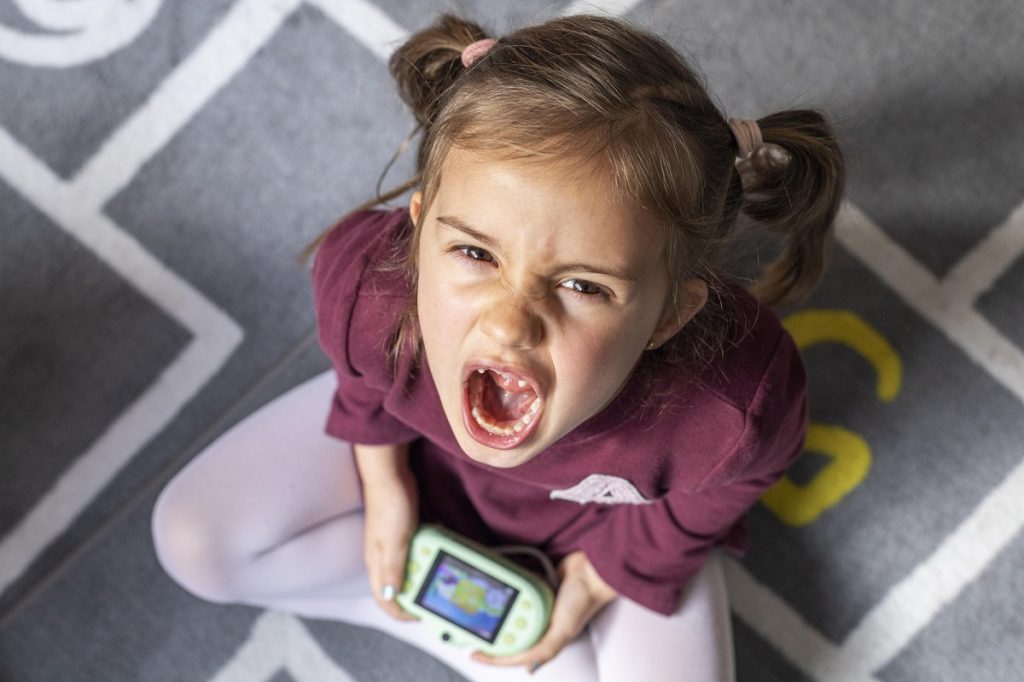 upset toddler screaming while sitting on the floor and holding a toy
