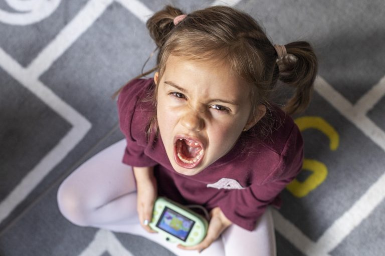 upset toddler screaming while sitting on the floor and holding a toy